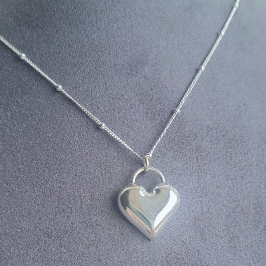 Silver heart-shaped pendant necklace on a mannequin bust.