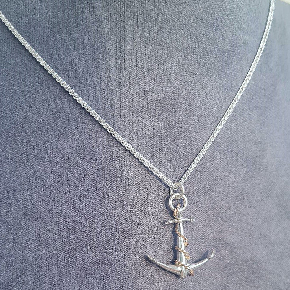 Silver anchor necklace with rose gold rope detail on a gray fabric background