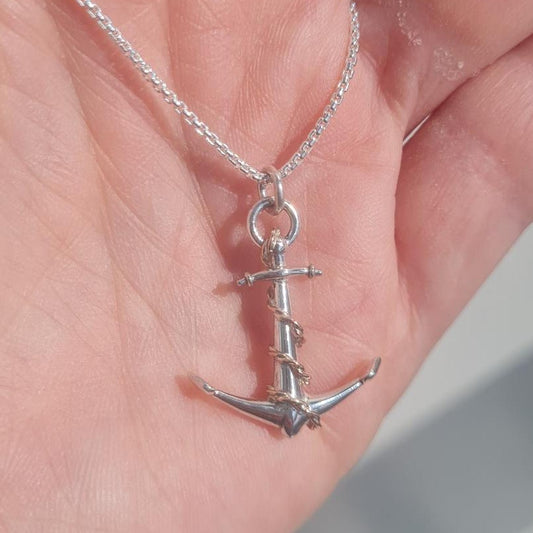A silver anchor pendant with 9ct rose gold on a necklace delicate chain, held in a person's hand.