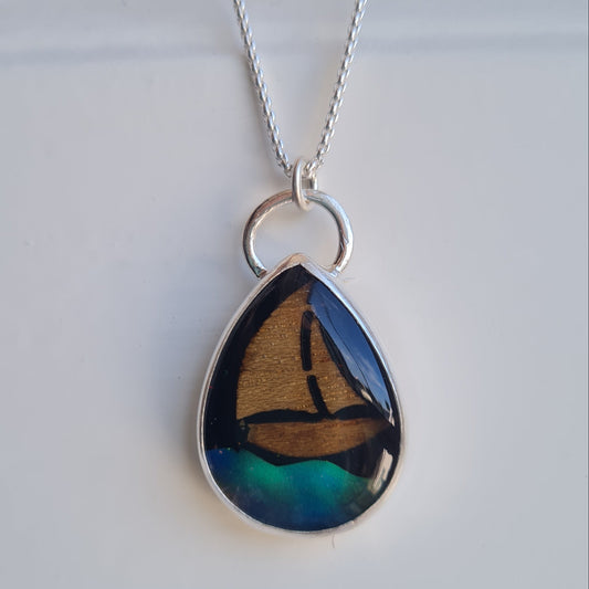 A silver teardrop pendant necklace featuring an iridescent aurora opal wave inlay with blue, green, and wood yacht inlay with black star sky background, suspended from a delicate silver chain