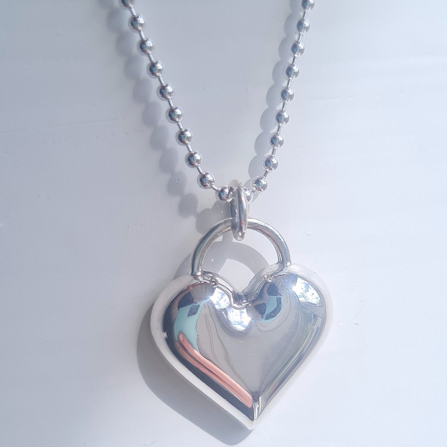 Silver heart-shaped pendant on a chain against a light gray background