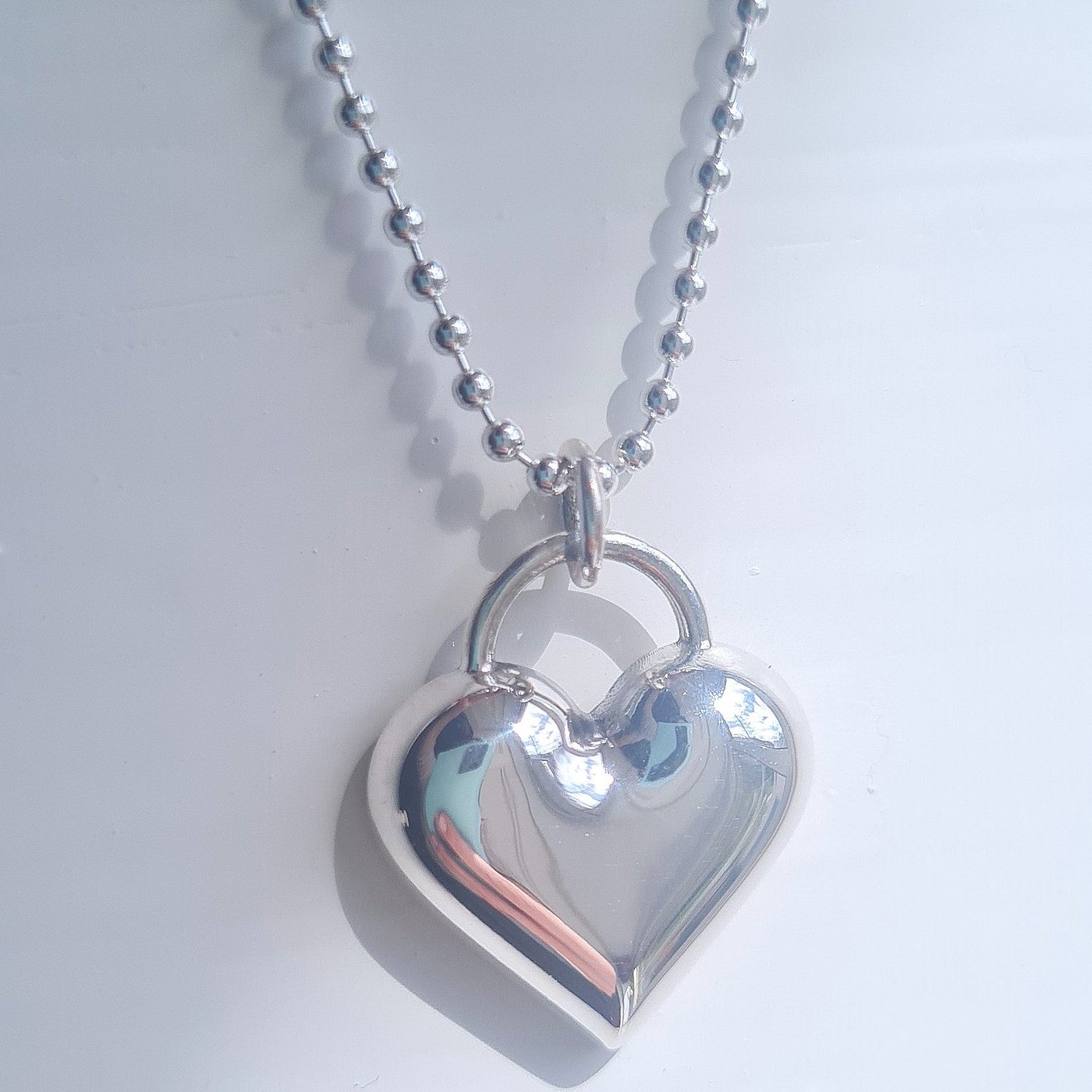 Silver heart-shaped pendant on a chain against a light gray background