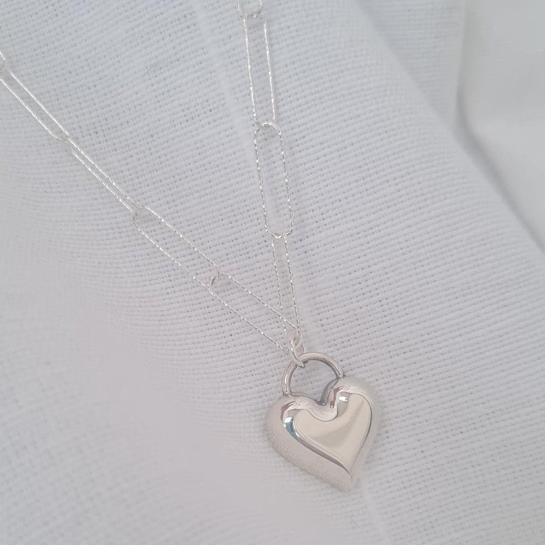 Silver heart-shaped pendant on a thin paperclip chain against a light grey background
