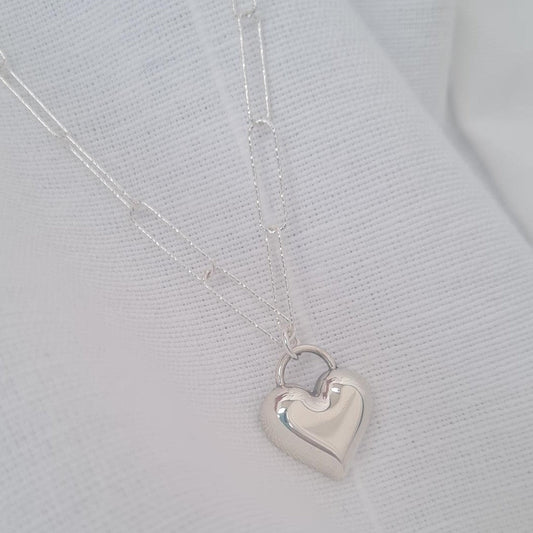 Silver heart-shaped pendant on a thin paperclip chain against a light grey background