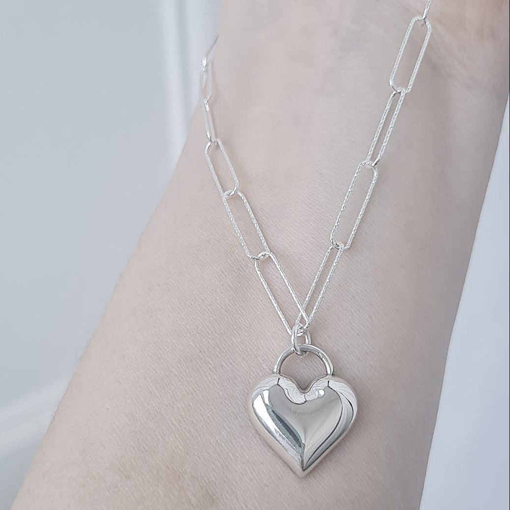 Silver heart-shaped pendant necklace on a person's wrist against a light background