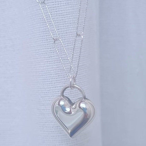 Silver heart-shaped pendant on a chain against a light gray background