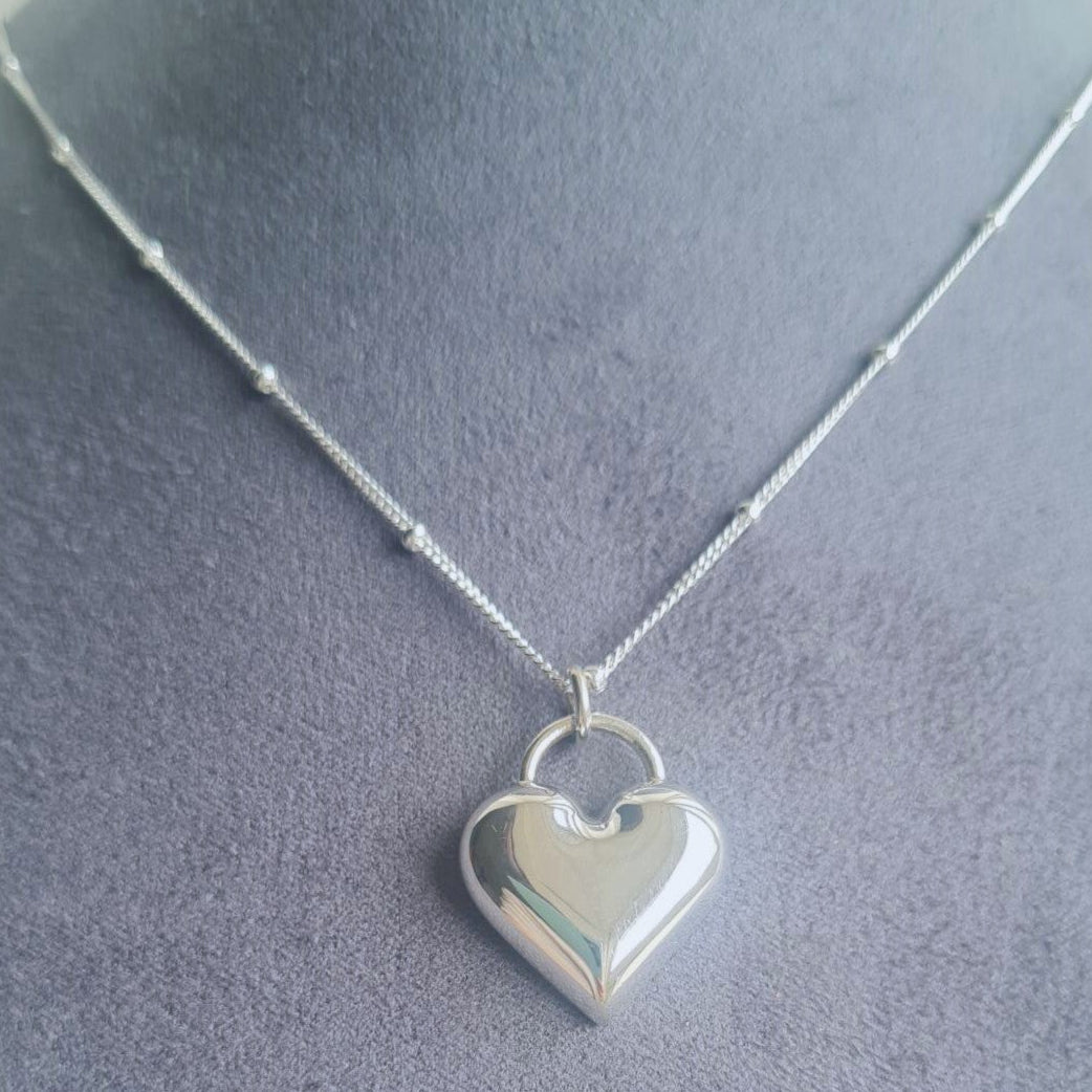 Silver heart-shaped pendant on a chain against a gray background