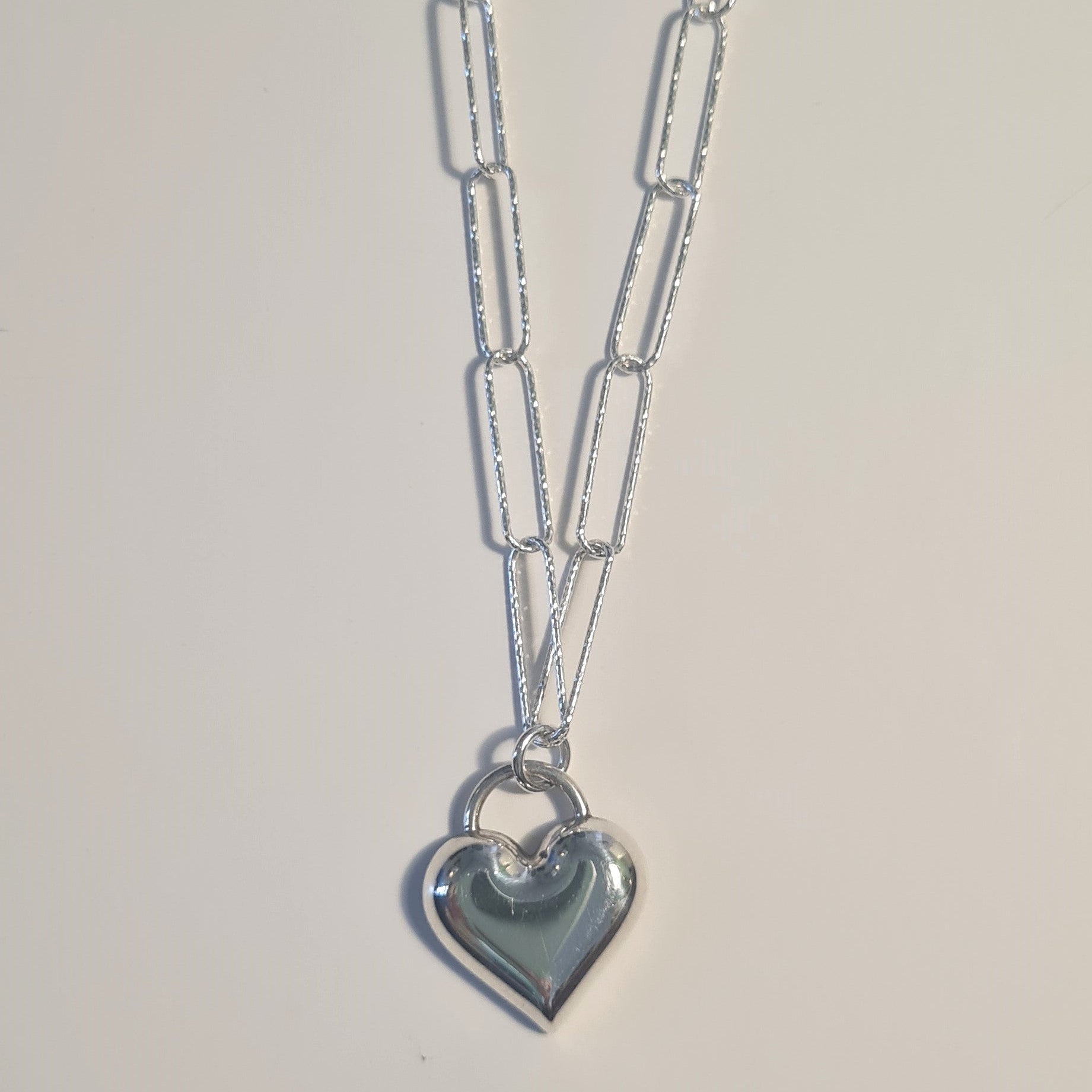 Silver necklace with a heart pendant on a light gray background