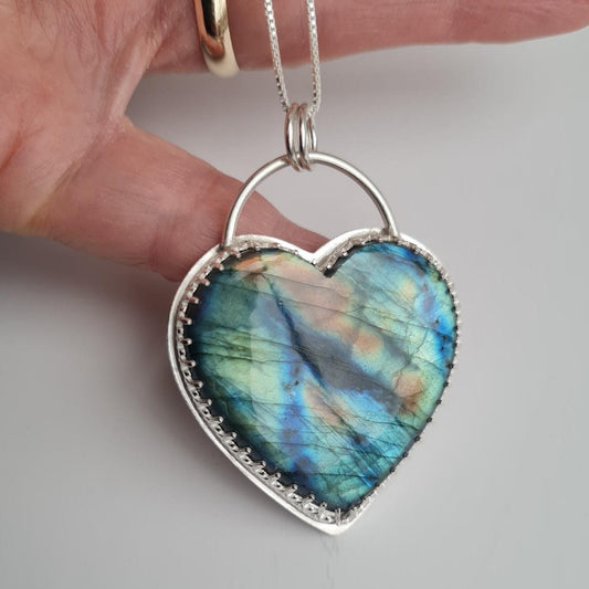 Heart-shaped labradorite pendant on a silver chain held by a hand.