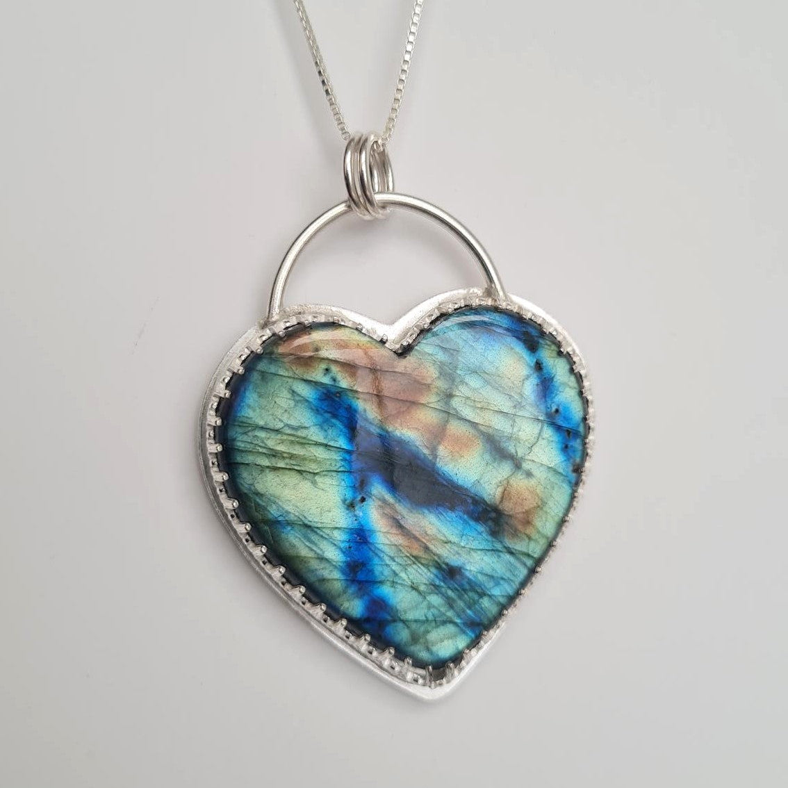 Heart-shaped labradorite pendant on a silver chain with blue green and yellow iridescence