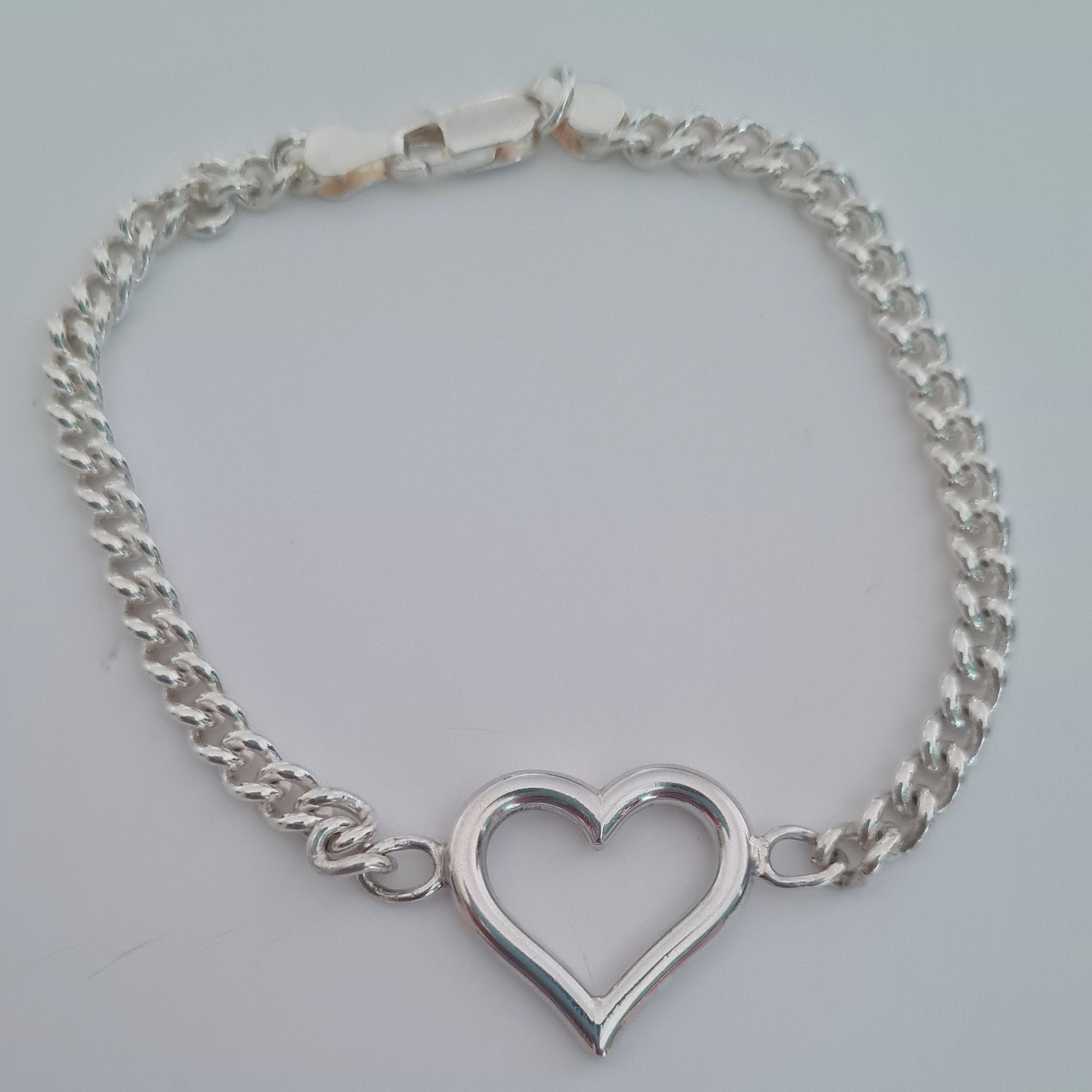 Silver bracelet with a heart-shaped charm on a light gray background