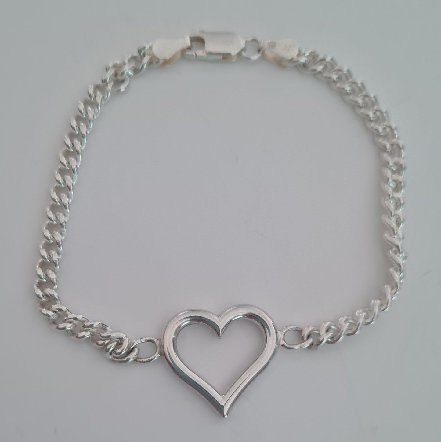 Silver chain bracelet with a heart-shaped clasp on a light gray background