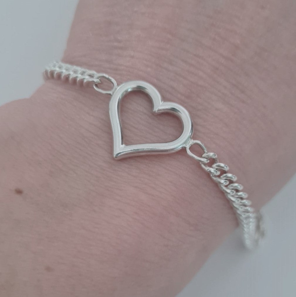 Silver heart-shaped bracelet on a wrist against a neutral background