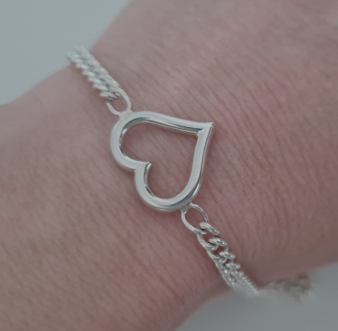 Silver heart-shaped bracelet on a wrist against a neutral background
