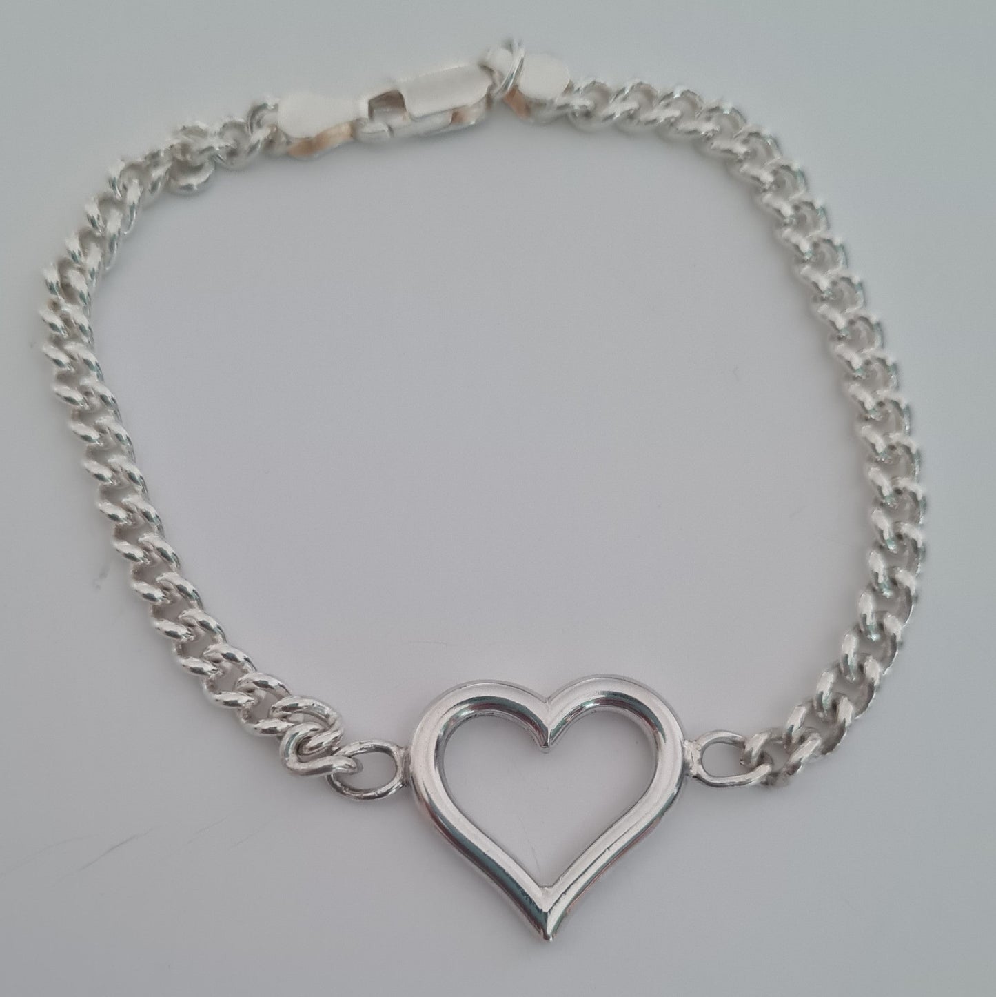 Silver chain bracelet with a heart-shaped clasp on a light gray background