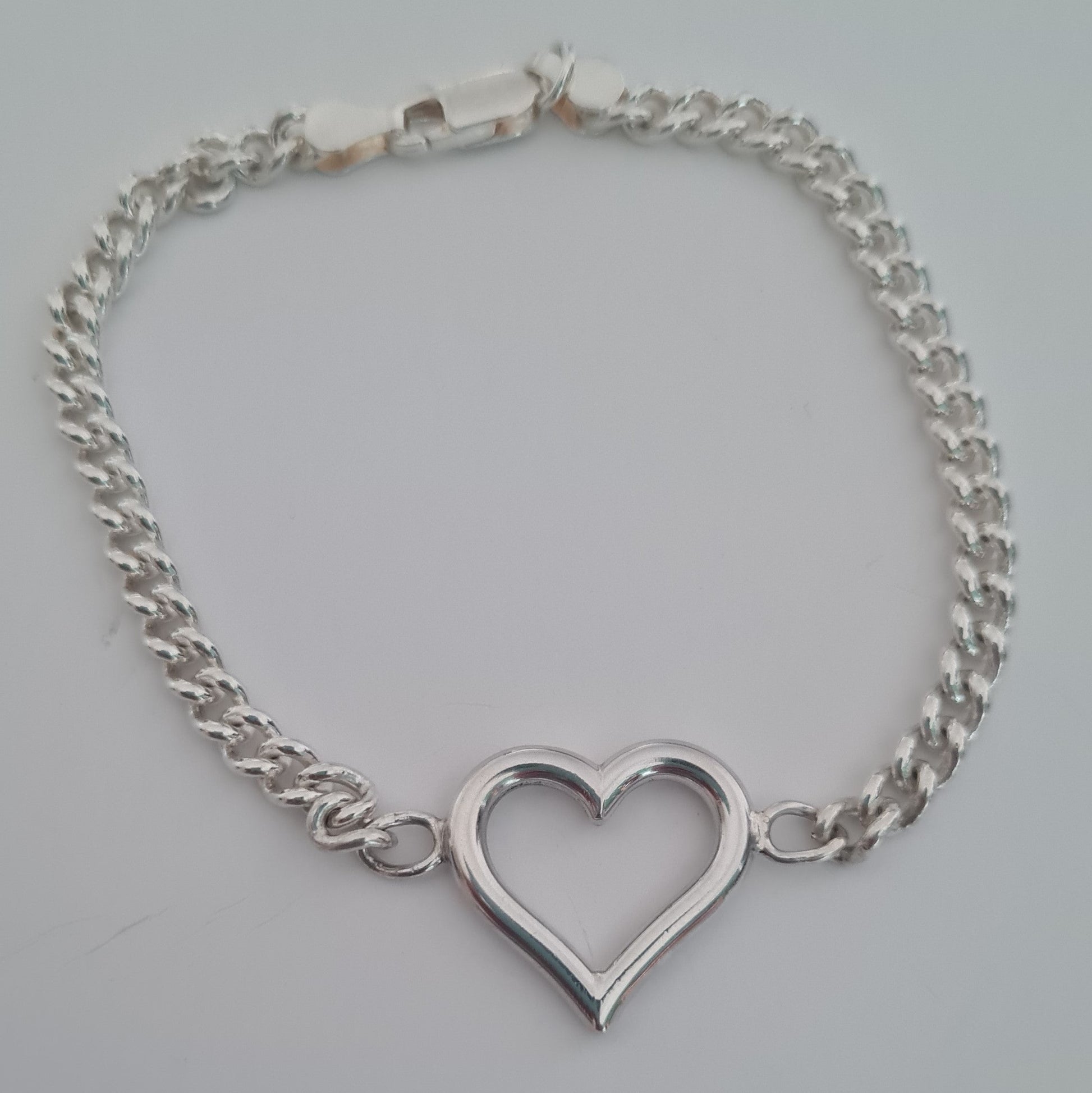 Silver chain bracelet with a heart-shaped clasp on a light gray background