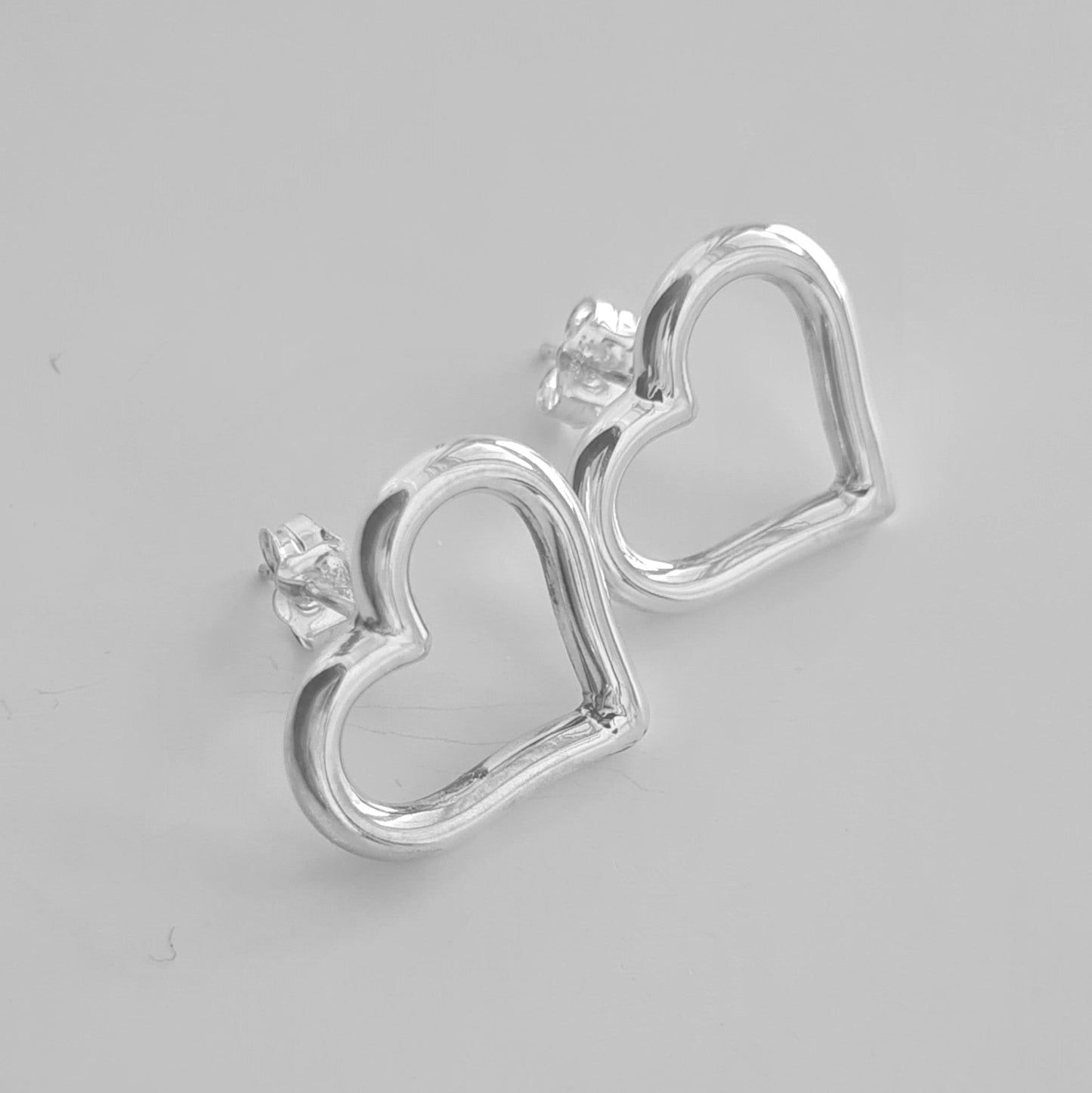 Silver heart-shaped stud earrings on a gray background