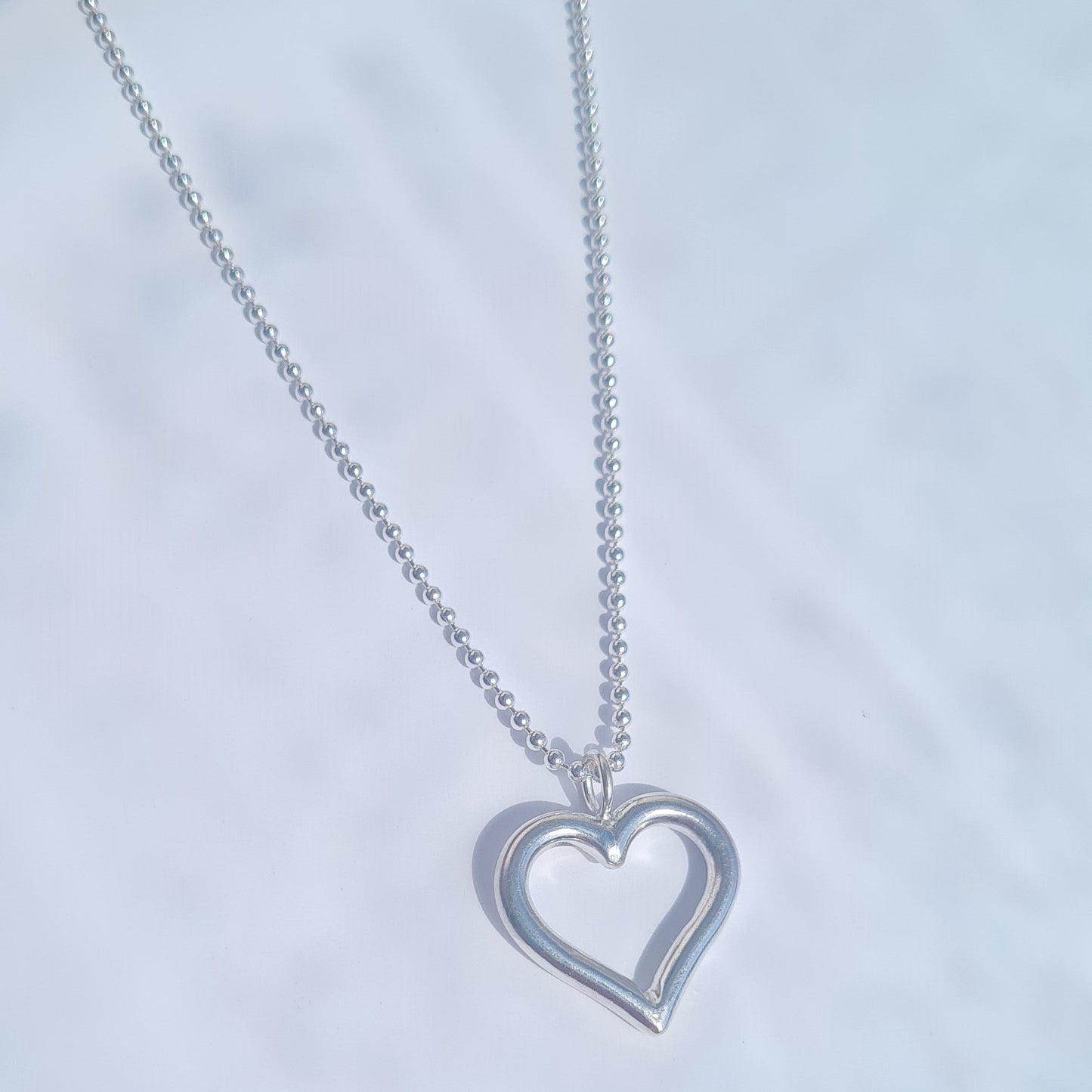 Silver heart-shaped pendant necklace on a light gray background