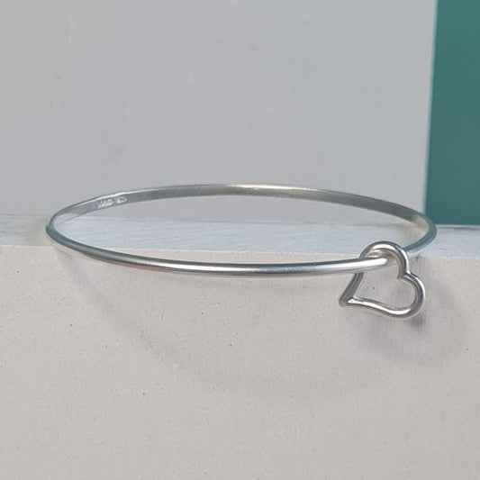 A thin silver bangle with silver heart charm 