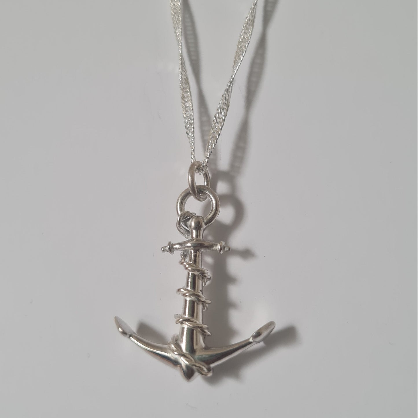 A silver anchor pendant necklace on a matching silver chain, displayed against a plain light gray background.