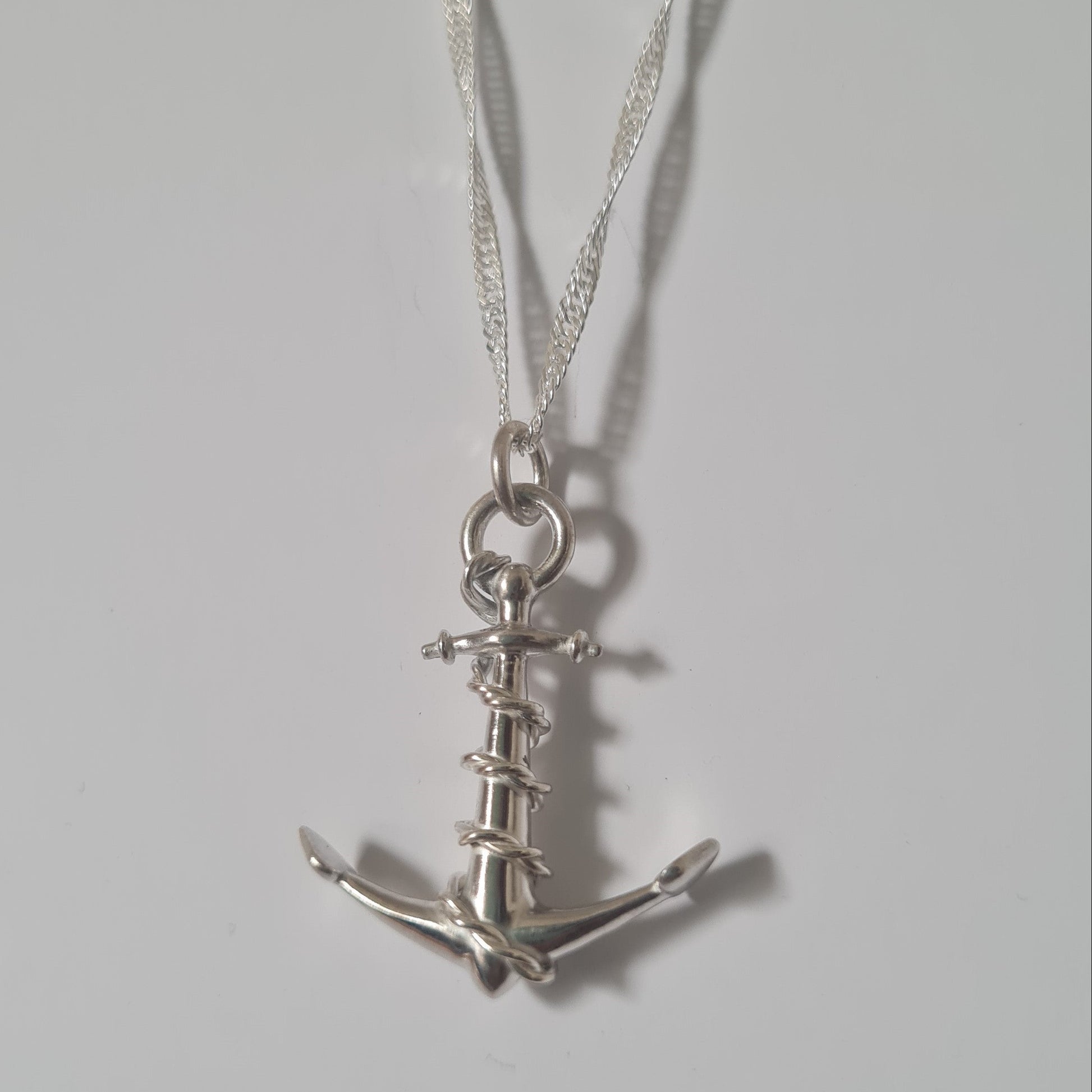 A silver anchor pendant necklace on a matching silver chain, displayed against a plain light gray background.