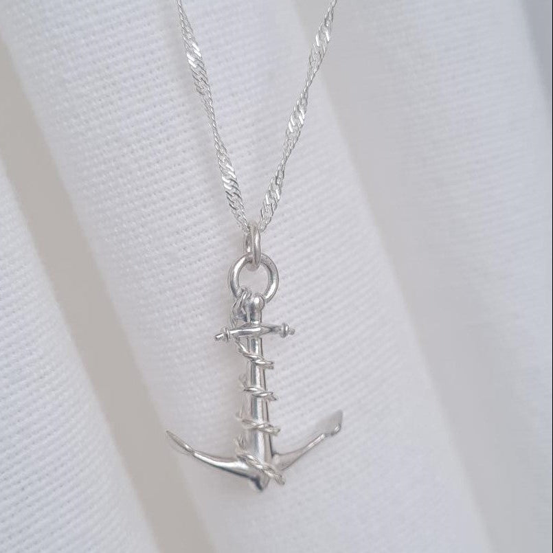 A silver anchor pendant necklace on a twisted silver chain, displayed on a white fabric bust.