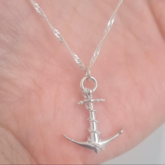 A silver anchor pendant necklace on a twisted chain, held in the palm of a hand.