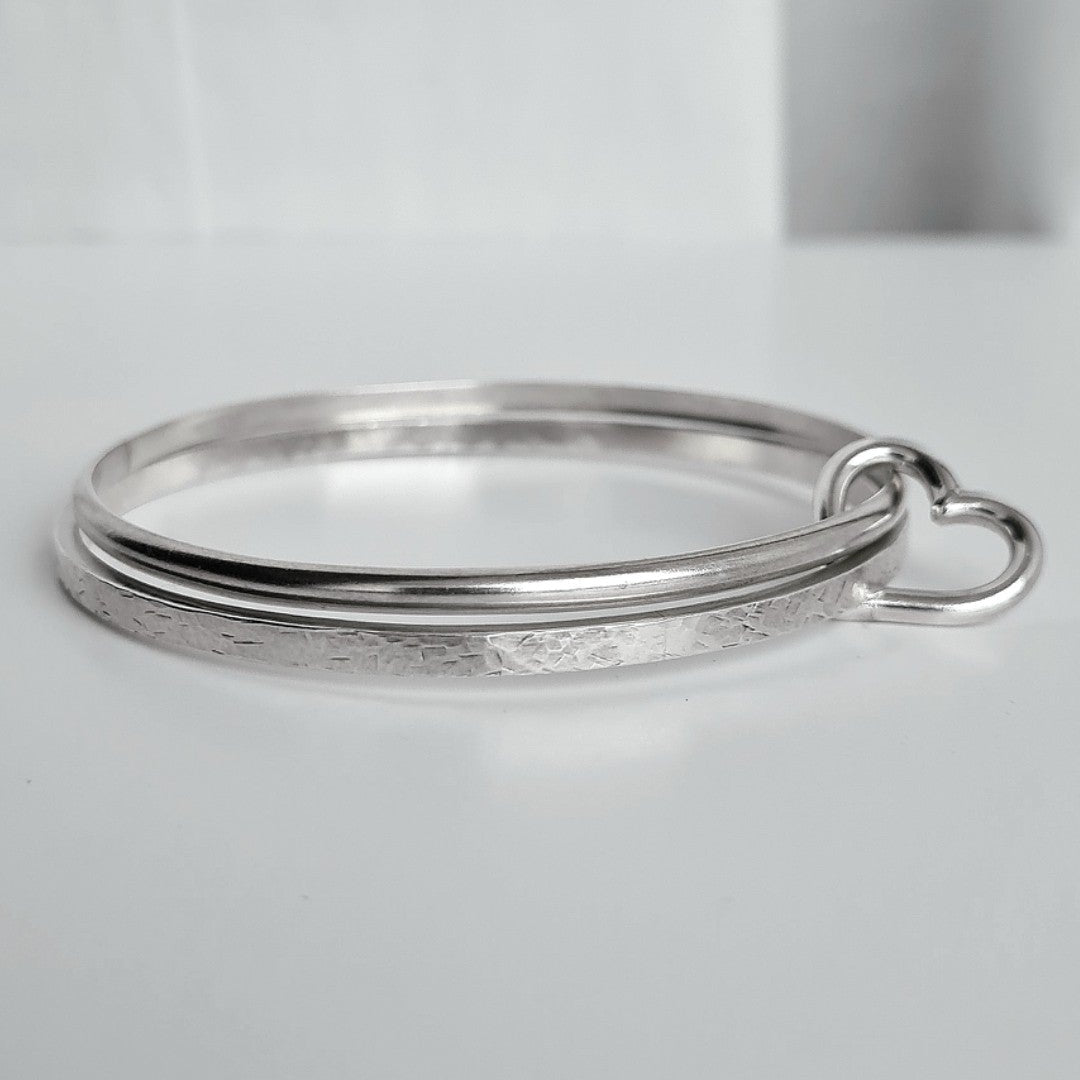 Two silver bangles linked with silver heart charm