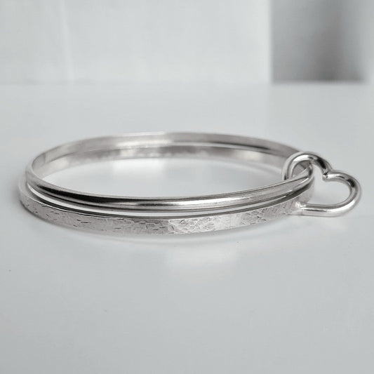Two silver bangles linked with silver heart charm