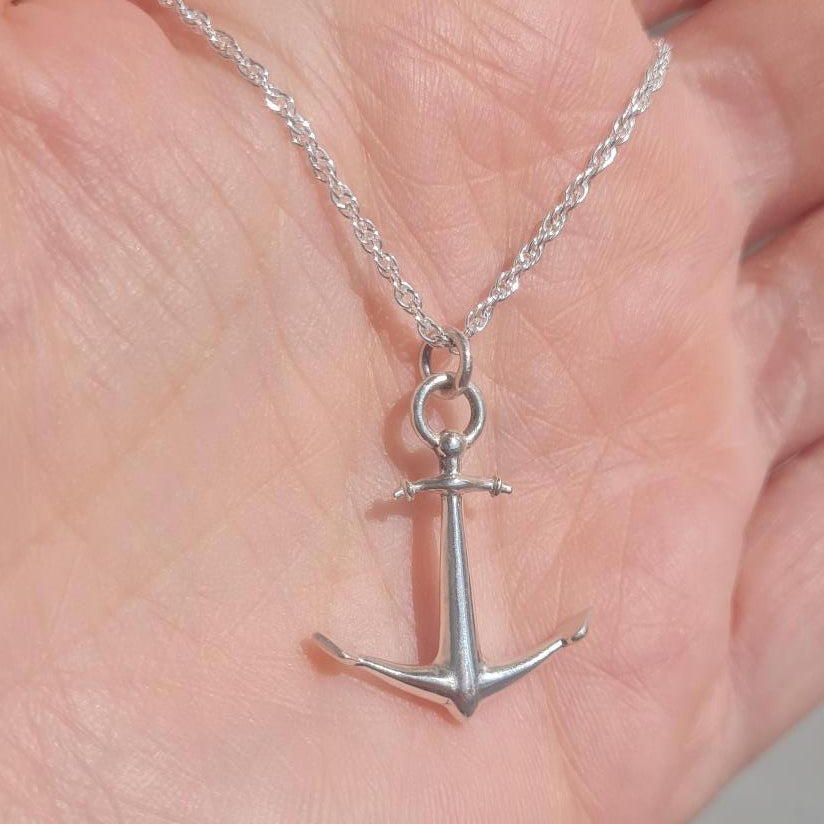A silver anchor pendant necklace on a delicate silver chain, resting on an open hand to show scale.